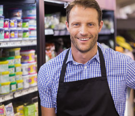 Trabajador de un supermercado sonriendo con yogures de fondo