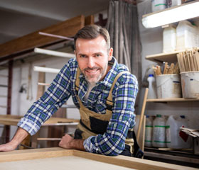 Hombre carpintero apoyando en una mesa y sonriendo